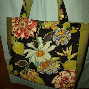 May include: A black tote bag with green trim and a floral print featuring daisies, lemons, and other flowers in shades of red, yellow, blue, and green.
