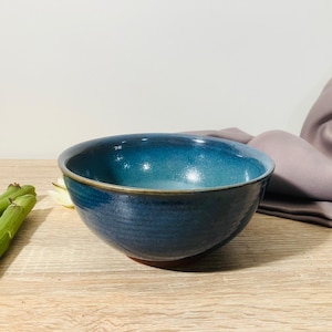 Peut inclure: Un bol en céramique fait à la main avec un dégradé de bleus, allant d'un indigo profond à un turquoise plus clair. Le bol a une finition lisse et brillante et un bord marron. Des asperges sont visibles sur une surface en bois.