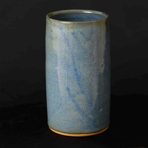 Peut inclure: Un vase en céramique bleu avec un glaçage bleu clair et blanc. Le vase a un fond arrondi et un corps cylindrique droit.