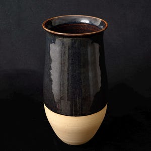 Peut inclure: Un vase en céramique bleu foncé avec un bord et une base brun clair. Le vase a une finition lisse et brillante.