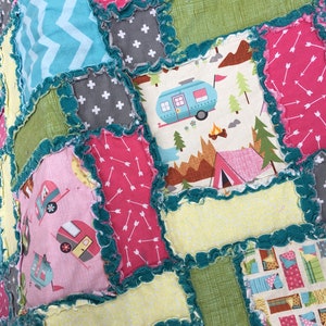 May include: A patchwork quilt with a camping theme. The quilt is made of various fabrics, including pink, green, blue, and yellow. The quilt features a variety of camping-related images, including campers, tents, and trees. The quilt is edged with a teal ruffled trim.