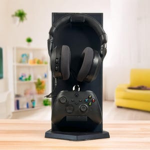Könnte beinhalten: Ein schwarzer Gaming-Headset- und Controller-Ständer mit einem schwarzen Headset und einem schwarzen Controller. Der Ständer steht auf einem Holztisch.