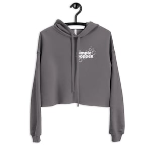 May include: A charcoal gray cropped hoodie with a white graphic of the text "Simple Popper" with a circle around the "O" in "Popper" and three white circles around the text.
