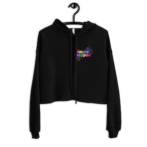 May include: Black cropped hoodie with a rainbow colored "Simple Popper" logo on the front. The logo is surrounded by small circles.