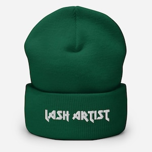Puede incluir: Un gorro de lana verde oscuro con un logotipo bordado en blanco que dice "LASH ARTIST".