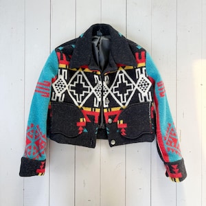 May include: A cropped wool jacket with a Southwestern design. The jacket has a black body with turquoise sleeves and a collar. The design includes geometric patterns in red, yellow, and white. It has two front pockets and silver buttons.