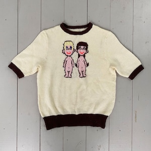 May include: A white knitted sweater with a brown trim and a cartoon image of a boy and girl. The sweater has short sleeves.
