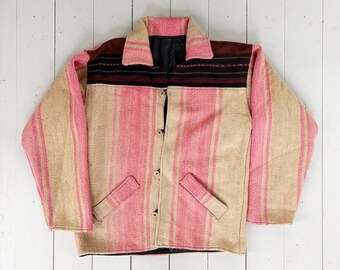 May include: A pink and tan striped jacket with a brown collar and accents. The jacket has a button-up front and two front pockets. The fabric appears to be woven, with a textured look. The jacket is laid flat on a white wooden surface.