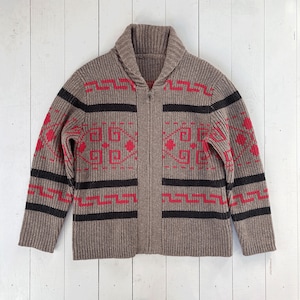 Puede incluir: Un cárdigan marrón con cremallera y cuello chal. El suéter presenta un patrón geométrico en rojo y negro, con rayas negras horizontales y formas geométricas rojas. El suéter está hecho de un material de punto acanalado.