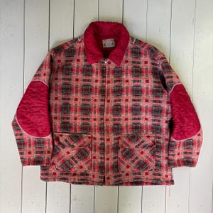 May include: A vintage jacket in a red, black, and grey plaid pattern, with a zip closure and two front pockets. It has quilted red elbow patches and a red collar. The collar tag reads "Truckman 1942".