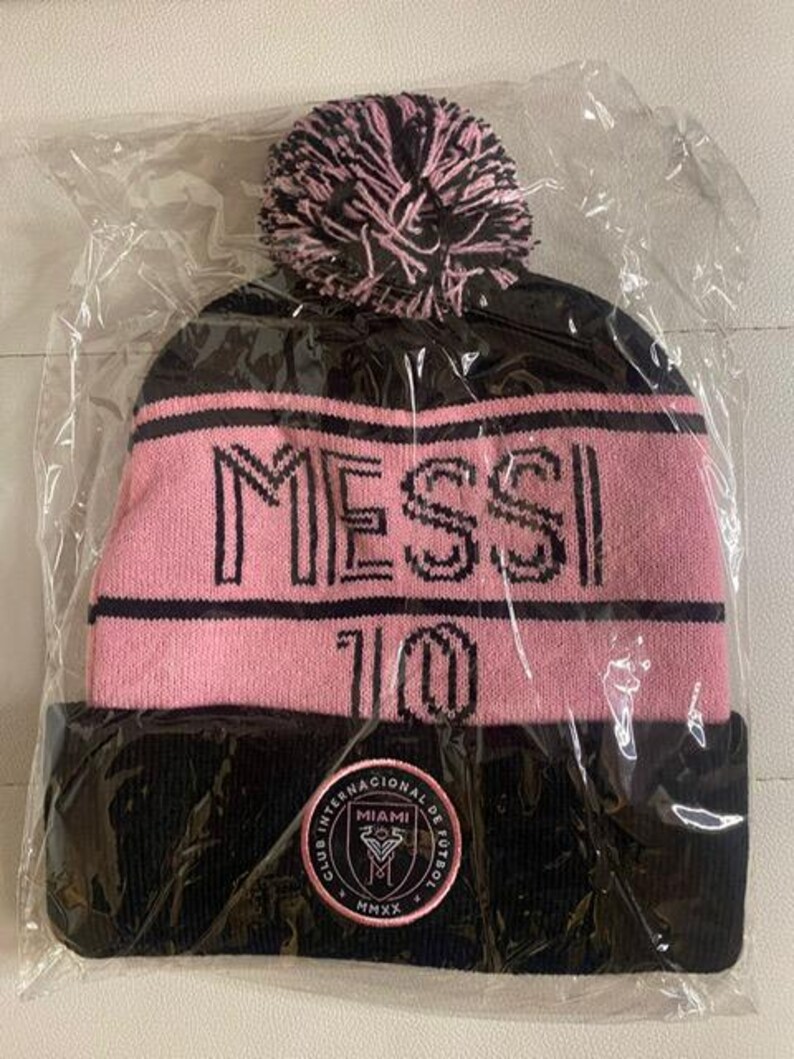 May include: Black and pink knit beanie with a pom pom on top. The beanie has the text "MESSI 10" on the front and a logo with the text "Club Internacional de Futbol Miami MMXX" on the back.