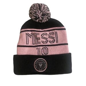 May include: Black and pink knit beanie with a pom pom on top. The beanie has the word "MESSI" and the number "10" on the front. The beanie also has a small logo on the bottom that says "Club Internacional de Futbol Miami 2025 MMXX".