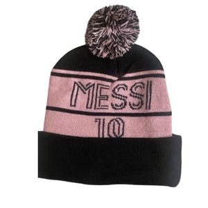 May include: Black and pink knit beanie with a pom pom on top. The beanie has the word "MESSI" and the number "10" embroidered on the front.