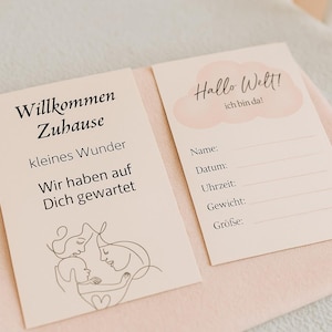 Op de afbeelding: Twee lichtroze baby aankondigingskaarten met Duitse tekst. Eén kaart leest "Willkommen Zuhause" en de andere zegt "Hallo Welt! ich bin da!". De kaarten hebben ruimte om de naam, datum, tijd, gewicht en grootte van de baby te schrijven.
