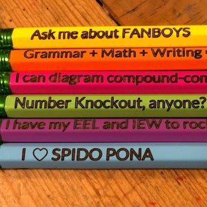 May include: A set of six colorful pencils with different phrases written on them. The phrases are: "Ask me about FANBOYS", "Grammar + Math + Writing = Essentials", "I can diagram compound-complex sentences.", "Number Knockout, anyone?", "I have my EEL and IEW to rock out my KWO.", and "I SPIDO PONA".