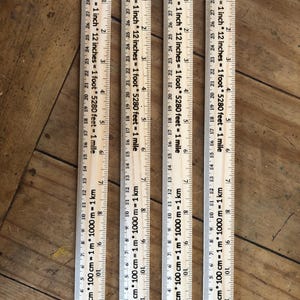 May include: Wooden rulers with inch and centimeter markings. Each ruler is 12 inches (30.48 cm) long and features conversions: 2.54 cm = 1 inch, 12 inches = 1 foot, and 5280 feet = 1 mile. The rulers are on a wooden surface.