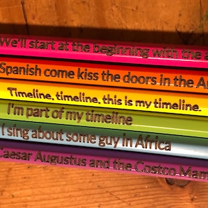 May include: A stack of colorful pencils with text. The pencils are in shades of pink, orange, yellow, green, blue, and purple. Each pencil has a different phrase written on it in a brown font.