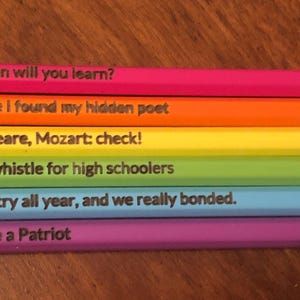 May include: A collection of six pencils in a rainbow of colors, each with a different quote printed on the side. The pencils are arranged horizontally, with the text visible. The quotes are related to literature, music, and history.