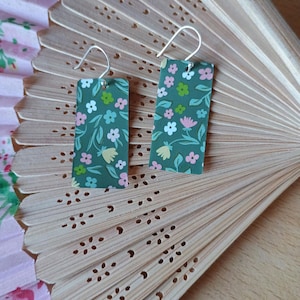 May include: A pair of green rectangular earrings with a floral pattern. The earrings have silver hooks.