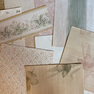 May include: A collection of overlapping wallpaper samples featuring various designs including a floral border with green and purple foliage, a small orange and green diamond pattern, a large beige floral print, and textured light green wood grain.