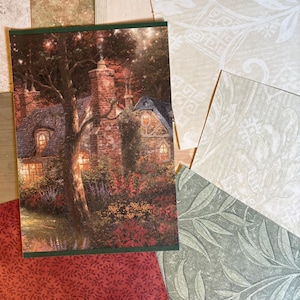 May include: A rectangular print featuring a stone cottage with a chimney, glowing windows, and a garden, surrounded by several overlapping paper samples with various patterns including red floral, green leaf, and cream damask designs.