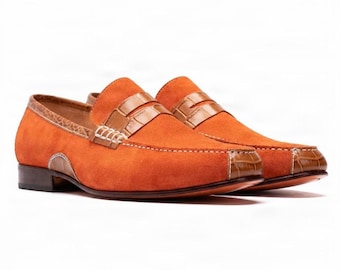 Könnte beinhalten: Ein Paar orangefarbene Wildleder-Loafer mit braunen Akzenten aus Leder in Krokodilprägung an der Spange, der Ferse und der Schuhspitze. Die Schuhe haben einen flachen Absatz, sichtbare weiße Nähte und eine dunkelbraune Sohle.