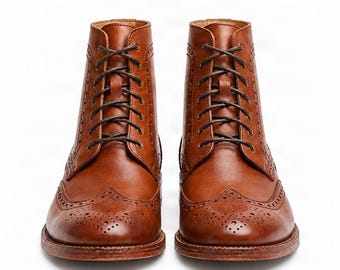 May include: A pair of tan leather lace-up boots featuring a wingtip toe cap with decorative brogue perforations. The boots have a high-top silhouette, dark brown laces, and a stacked leather heel, showcasing a classic construction and smooth finish.