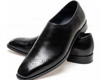 Könnte beinhalten: Ein Paar schwarze Lederschuhe mit poliertem Finish, quadratischer Zehenpartie und dekorativen Brogue-Perforationen an der Zehenkappe und am Schaft. Die Schuhe haben einen niedrigen Absatz und eine elegante Slip-on-Konstruktion.