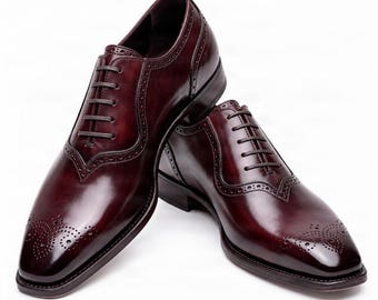 May include: A pair of polished dark burgundy leather oxford shoes featuring a wingtip design with intricate brogue detailing on the toe cap and along the seams. The shoes have a closed lacing system with thin dark brown laces and a low heel.