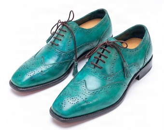 May include: A pair of teal green leather oxford shoes featuring a wingtip design with intricate brogue detailing, dark brown laces, and small decorative tassels attached to the eyelet area, set on a dark brown sole with a low stacked heel.