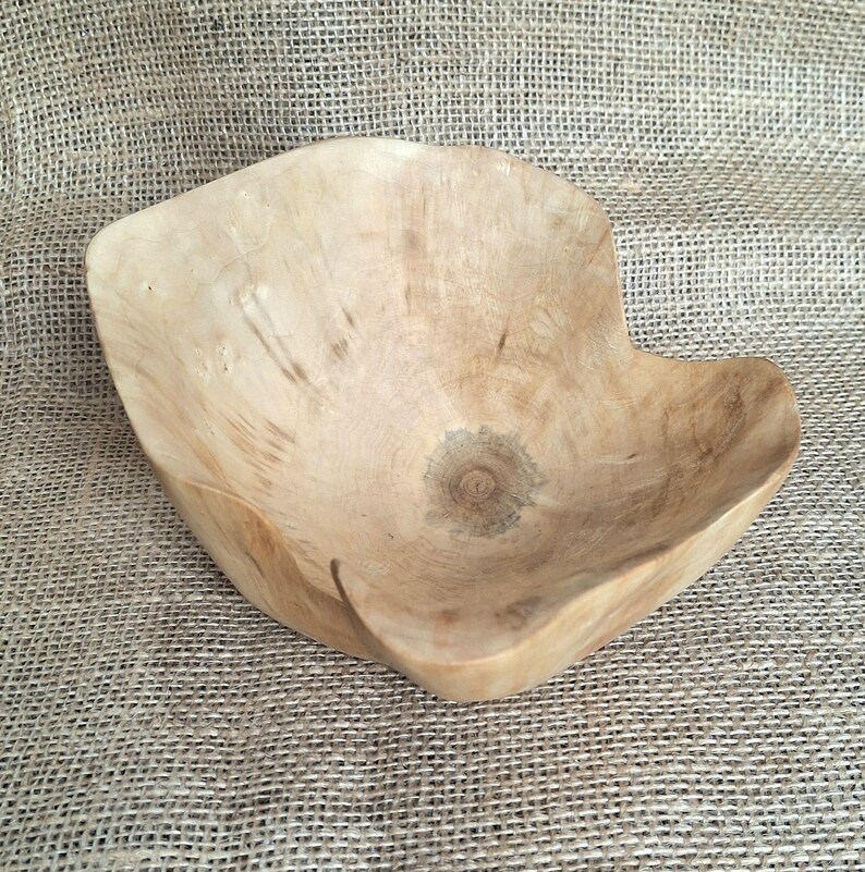 Op de afbeelding: Een handgemaakte houten kom met een unieke, organische vorm. De kom is gemaakt van lichtgekleurd hout, dat de natuurlijke nerf en textuur laat zien. Het ontwerp van de kom heeft een afgeronde binnenkant en een licht onregelmatige rand.