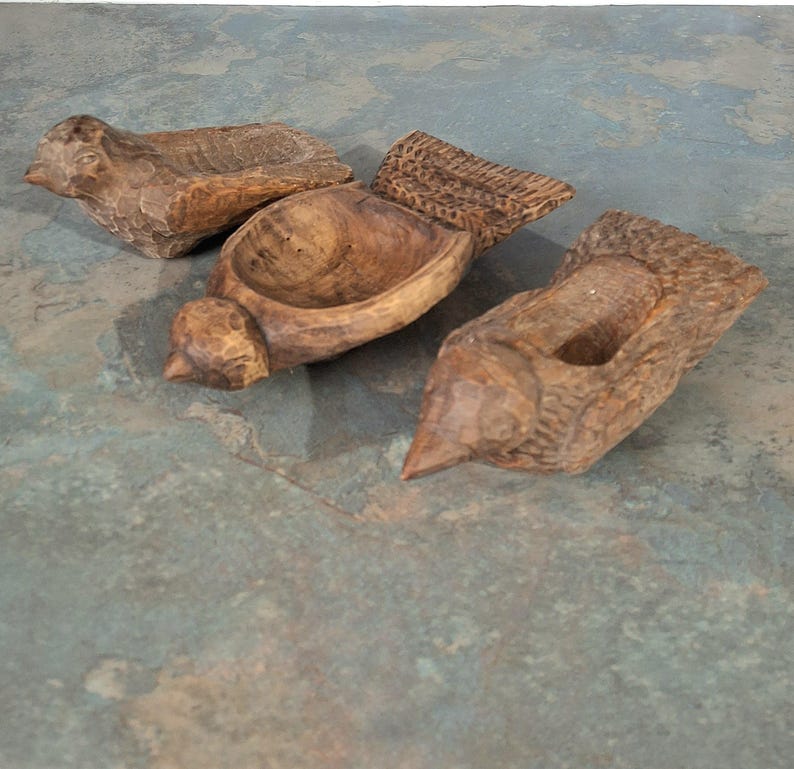 Pu&ograve; includere: Tre ciotole di legno intagliate a mano a forma di uccello. Le ciotole sono marroni con una superficie strutturata e ognuna ha un centro scavato. Gli uccelli hanno dettagli, tra cui becchi e ali intagliate.