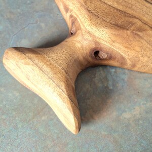 May include: Close-up of a handcrafted wooden serving board with a natural, organic shape. The board features a light brown colour with visible wood grain and a handle-like extension. The surface is smooth, showcasing the natural beauty of the wood.