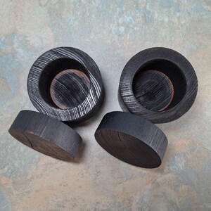 May include: Four pieces of dark grey wooden home decor. Two are circular with a bowl shape, and two are flat, oval-shaped. The wood grain is visible, and the pieces have a rustic, handmade appearance.