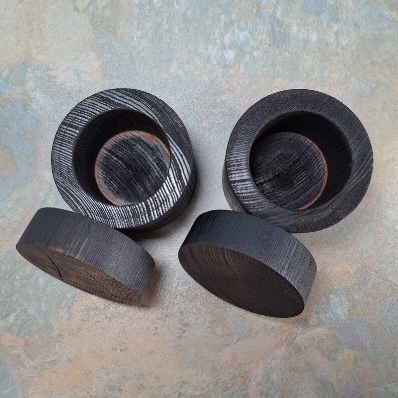 May include: Four pieces of dark grey wooden home decor. Two are circular with a bowl shape, and two are flat, oval-shaped. The wood grain is visible, and the pieces have a rustic, handmade appearance.