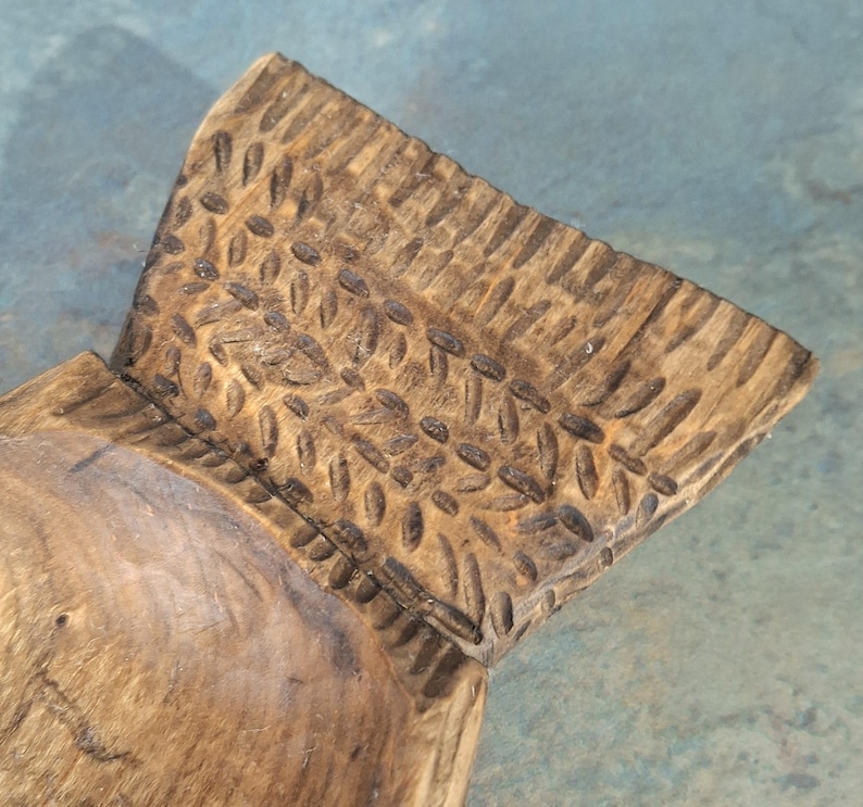 Pu&ograve; includere: Primo piano di una ciotola di legno intagliata a mano. La ciotola ha una finitura naturale con venature del legno e un design strutturato e modellato sul bordo. L'interno della ciotola &egrave; liscio, in contrasto con l'esterno dettagliato.