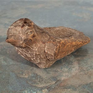 Pu&ograve; includere: Una ciotola a forma di uccello in legno intagliato. L'uccello &egrave; marrone con una superficie strutturata e un piccolo dettaglio dell'occhio. La ciotola &egrave; aperta nella parte superiore, creando uno spazio per piccoli oggetti. Il pezzo ha un aspetto rustico e artigianale.