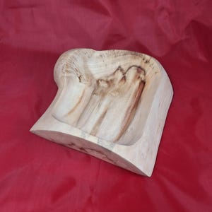 May include: A hand-carved wooden bowl with a natural, light finish and visible wood grain. The bowl has a unique, organic shape with a curved edge and a carved interior. The background is a solid red colour.