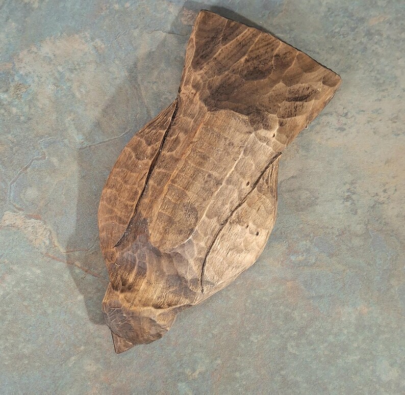 Pu&ograve; includere: Scultura in legno intagliata a mano di un uccello, con superficie strutturata e venatura naturale. La scultura &egrave; di colore marrone caldo e ha una forma unica e organica. La scultura dell'uccello &egrave; un oggetto decorativo.