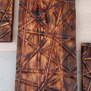May include: Three rectangular wooden wall art pieces with a geometric, carved design. The wood has a dark brown, burnt finish, with visible wood grain. The carved lines create a textured, dimensional effect, adding visual interest to the decor.