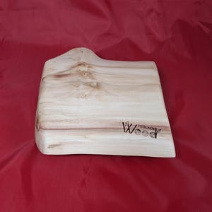 May include: A light-coloured wooden chopping board with a handle. The board has a natural wood grain pattern and a logo that reads "Wood Vizerunok". The board is on a red surface.