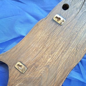 May include: A wooden wall hanging with a natural wood grain finish. The piece has a unique, organic shape and features two metal keyhole hangers and a drilled hole for mounting. The wood is a warm brown color.