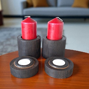 May include: A set of four wooden candle holders. Two cylindrical holders with red candles and two round tea light holders. The holders are dark brown and sit on a wooden table. The background includes a grey sofa.