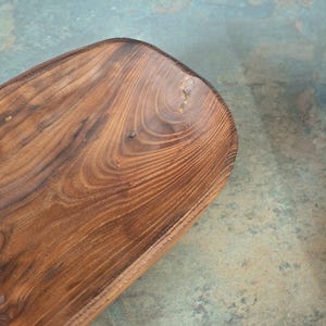May include: A handcrafted, wooden serving bowl with a rich, dark brown finish. The bowl has a rectangular shape with rounded corners and visible wood grain patterns. The natural wood tones and unique graining create a rustic aesthetic.