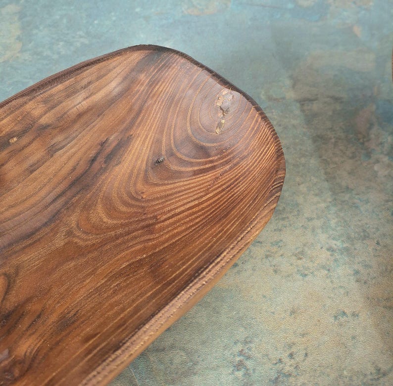May include: A handcrafted, wooden serving bowl with a rich, dark brown finish. The bowl has a rectangular shape with rounded corners and visible wood grain patterns. The natural wood tones and unique graining create a rustic aesthetic.