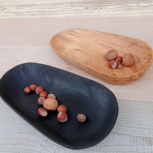 May include: Two wooden serving trays, one black and one natural wood, each holding nuts. The black tray has a dark, smooth finish, while the natural wood tray displays the wood grain. A rustic, natural theme.