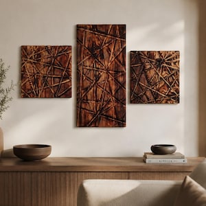 May include: Three wooden wall art panels with a textured, geometric design in shades of brown. The panels are rectangular and square, mounted on a neutral wall. A wooden console table below features a vase, bowl, and books, creating a warm, natural aesthetic.