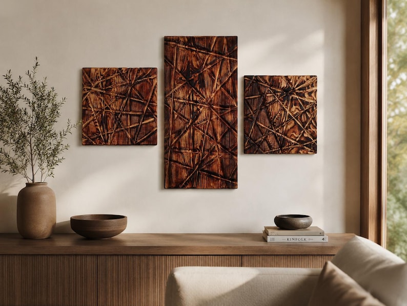 May include: Three wooden wall art panels with a textured, geometric design in shades of brown. The panels are rectangular and square, mounted on a neutral wall. A wooden console table below features a vase, bowl, and books, creating a warm, natural aesthetic.