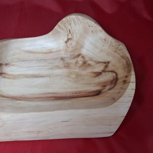 May include: A wooden bowl with a natural, light finish. The bowl has an organic shape with a raised edge. The wood grain is visible, enhancing its rustic appeal. It's likely for serving or display. The bowl's dimensions are in centimetres.