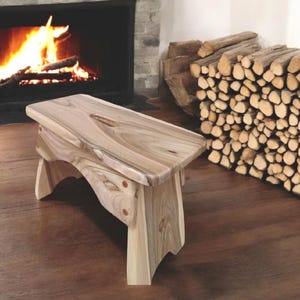 May include: A wooden stool with a natural wood finish and a curved design. The stool has a rustic look and is made from a single piece of wood.